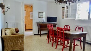 A dining area with a wooden table and red chairs, a television on a wooden desk, and a wicker sofa with cushions. - 400m from the beach, garden level with 1.250 m2 of enclosed land (Ramatuelle)