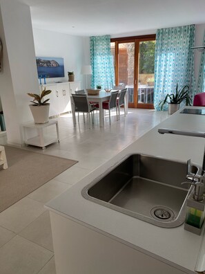Eine moderne Küche mit integriertem Spülbecken, ein Essbereich mit Tisch und Stühlen sowie Meerblick durch ein Fenster.
