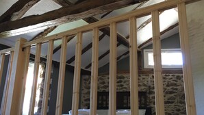 Un dormitorio con pared de piedra, estructura de cama de madera y techo inclinado con vigas a la vista.