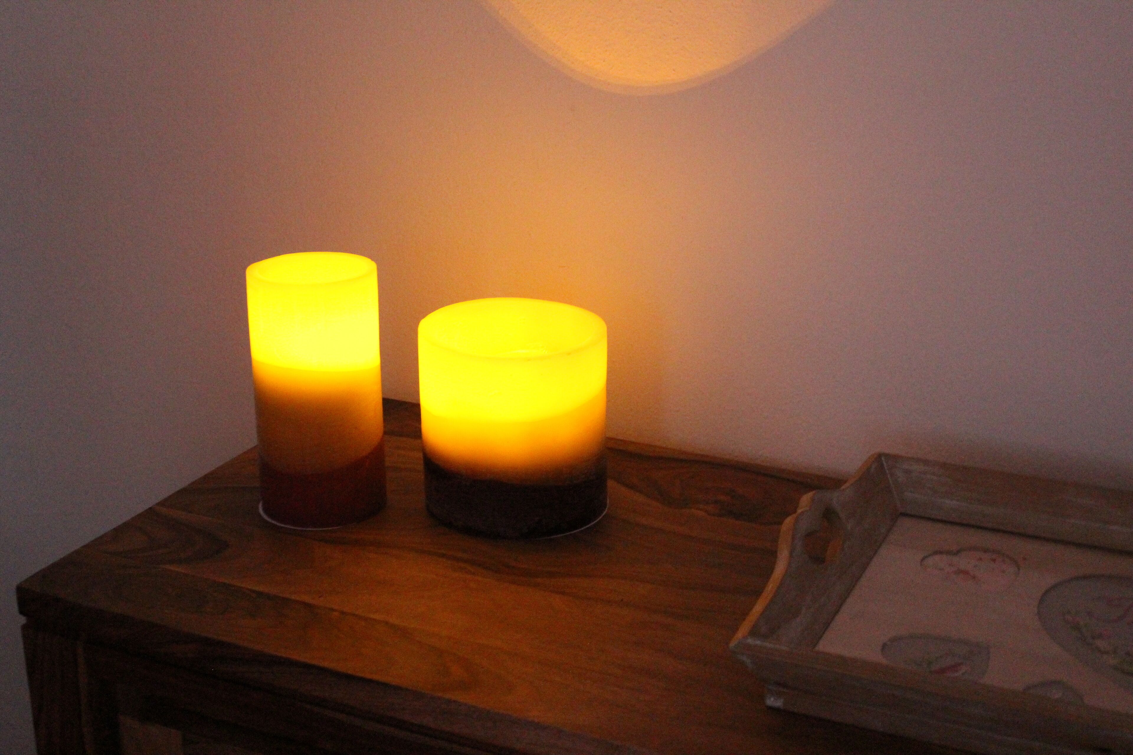 Two lit candles on a wooden table next to a framed picture.