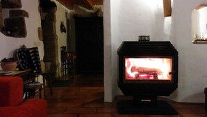 Een gezellige kamer met een houtkachel, een rode stoel en een stenen muur.