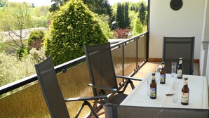 Un balcon avec une table dressée pour deux personnes, offrant une vue sur un jardin luxuriant et un grand arbre.