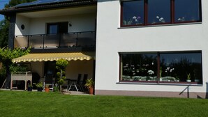 Une maison à deux étages dotée d’un balcon, de grandes fenêtres et d’un petit patio agrémenté de plantes en pot.