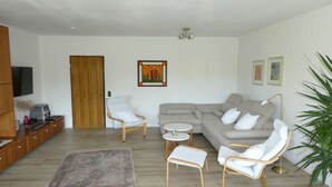 Un salon comprenant un canapé, deux fauteuils, une table basse, un tapis, un téléviseur et une porte.