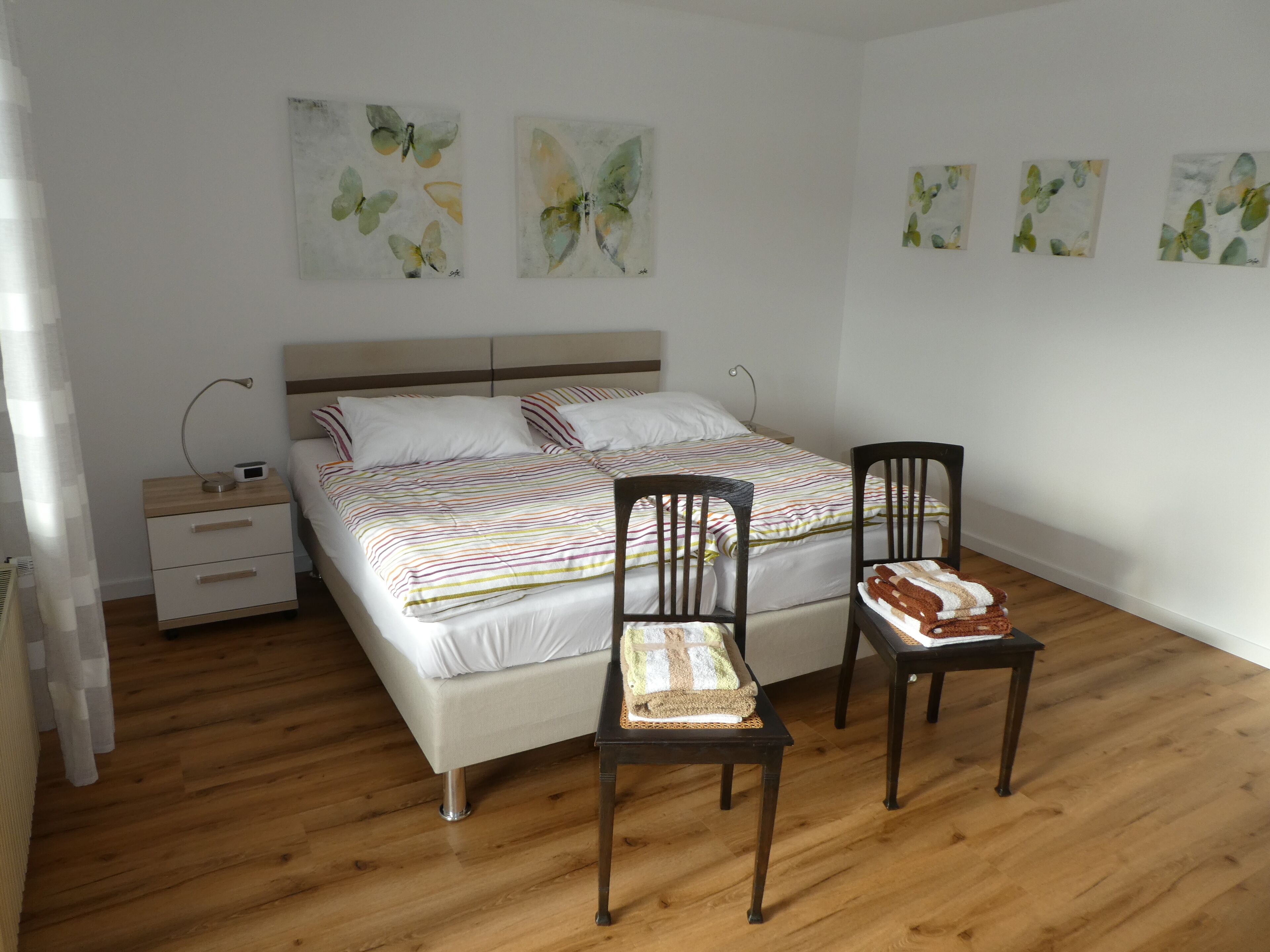 Ein Schlafzimmer mit einem Bett, zwei Stühlen, einem Nachttisch und einem Bild an der Wand.