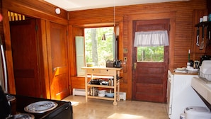 A kitchen with wooden walls, a stove, a sink, and a window with a view of trees.