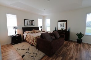 A bedroom with a bed, a brown sofa, a nightstand, a lamp, a potted plant, and a window with blinds. - Amazing Villa with south facing pool and conservation view (Davenport)