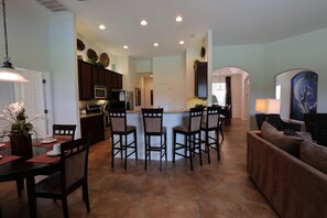 A spacious kitchen with dark wooden cabinets, a central island with bar stools, and a dining area with a table and chairs. - Amazing Villa with south facing pool and conservation view (Davenport)