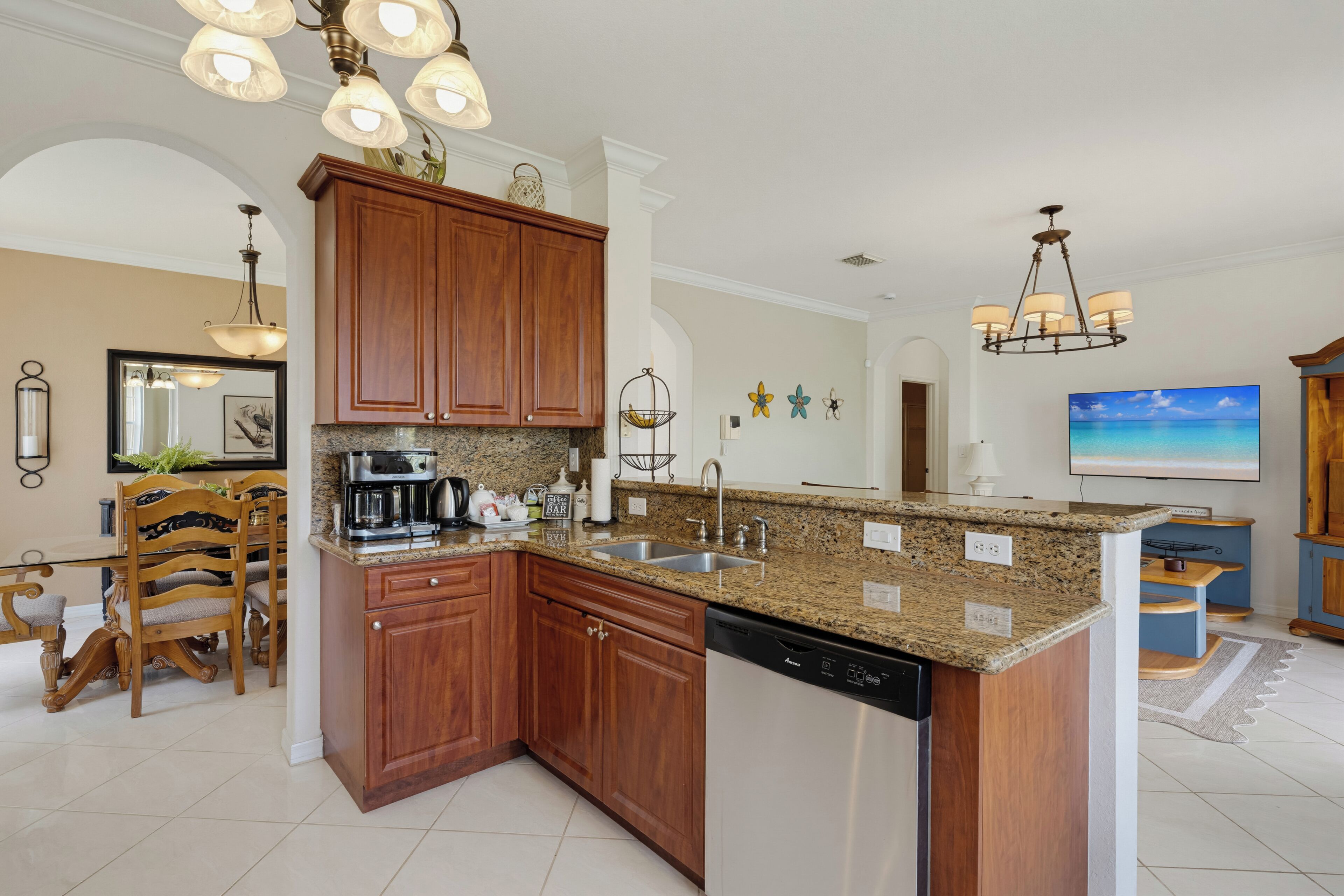A kitchen with granite countertops, wooden cabinets, a dishwasher, and a dining area with chairs and a table.
