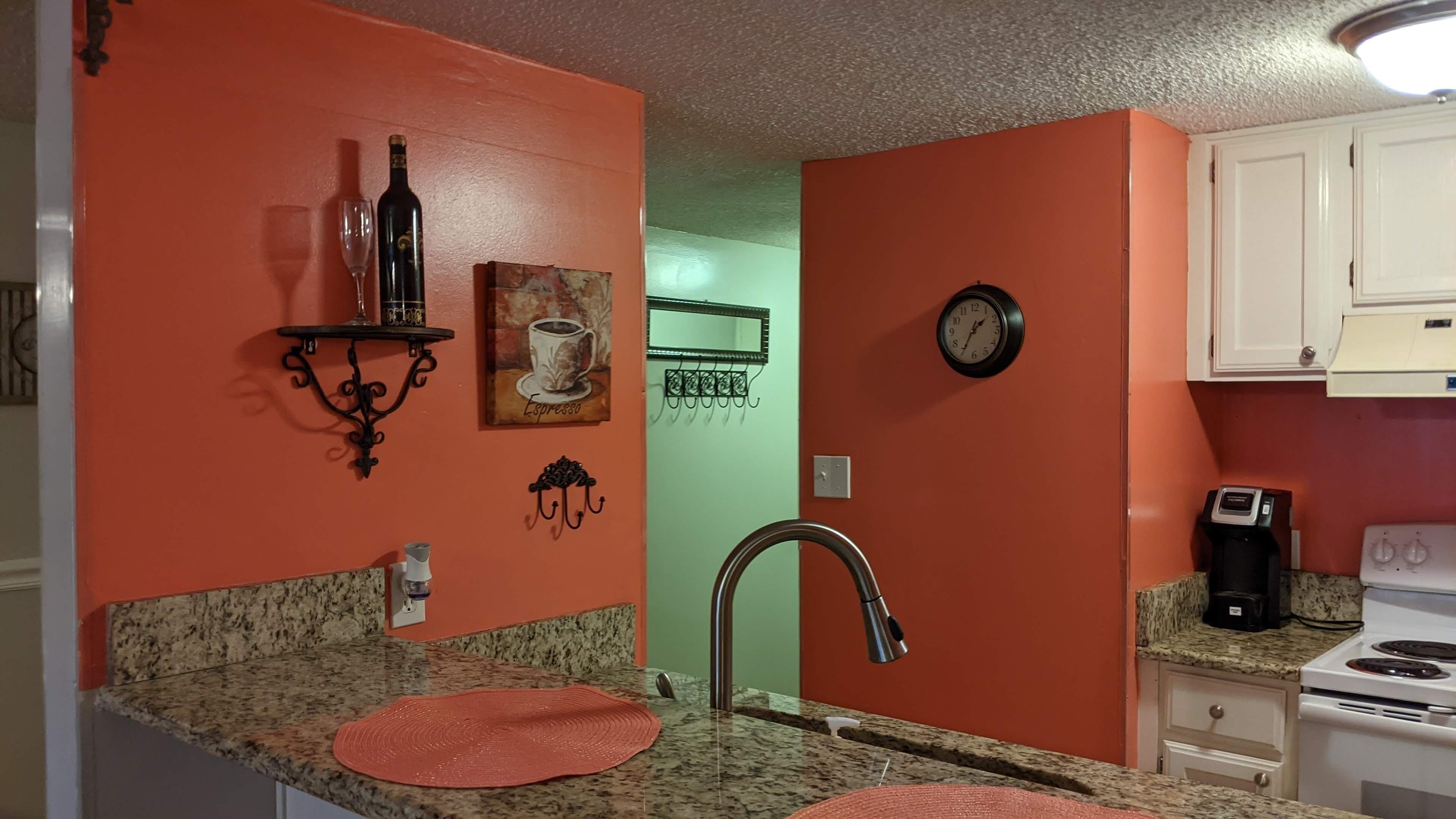 A kitchen with a granite countertop, a sink, a coffee maker, and a clock on the wall.