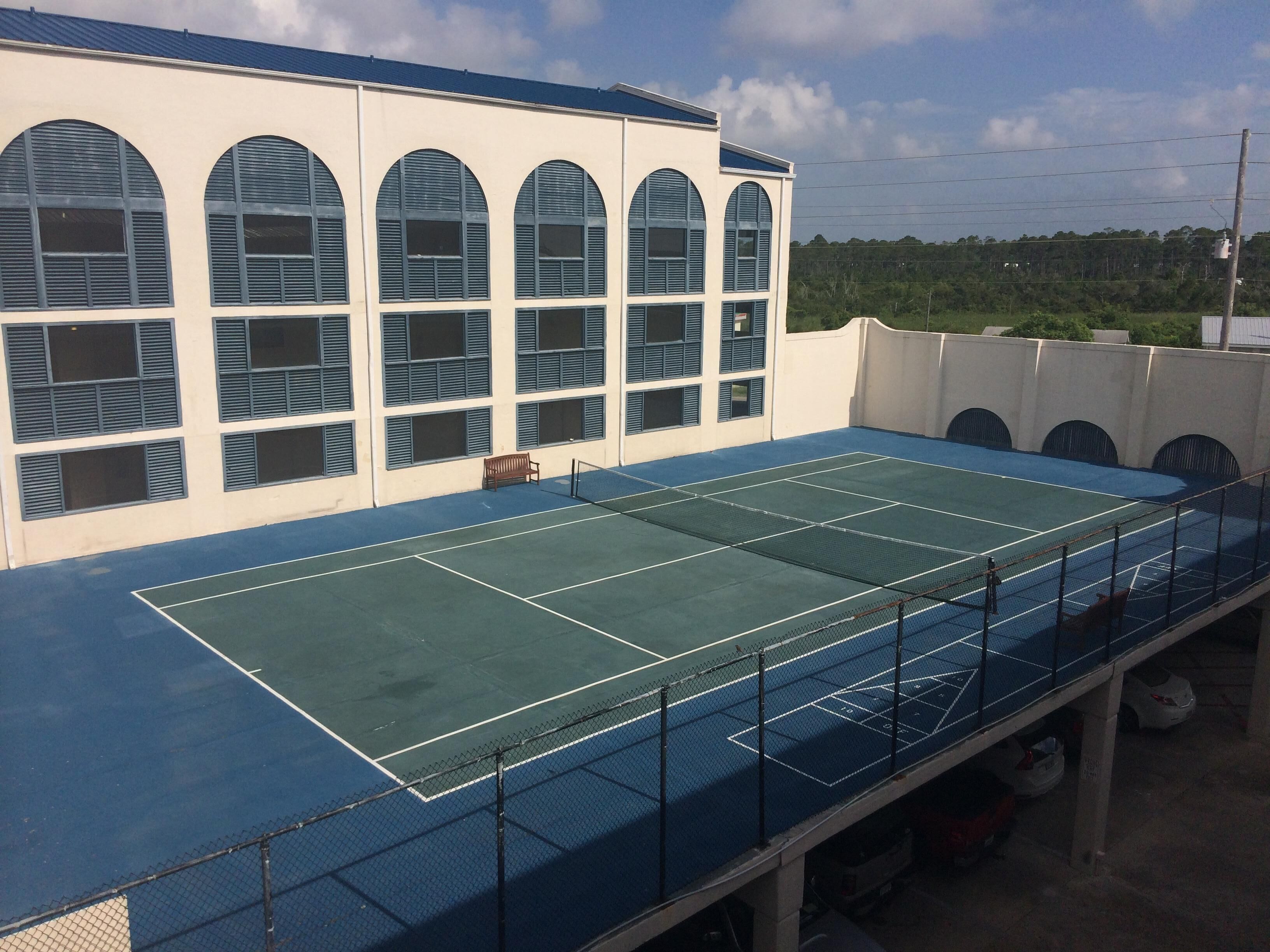 Un terrain de tennis avec un filet, des bancs et, au fond, un bâtiment doté de fenêtres en arc de cercle.