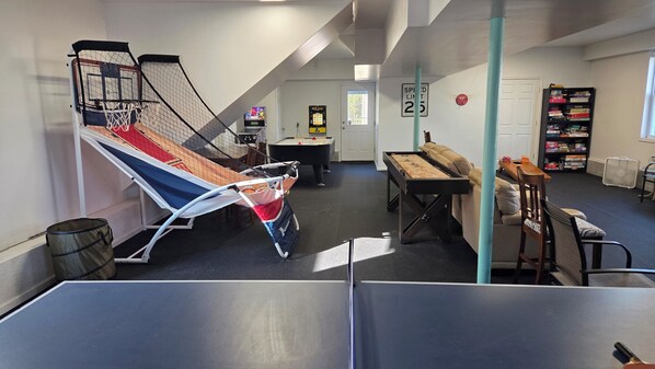 A room with a ping pong table, a foosball table, a pool table, a bookshelf, and a door with a speed limit sign.