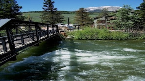 A wooden bridge over a flowing river with a mountain in the background.