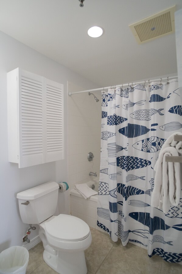 A bathroom with a toilet, a shower curtain with fish patterns, a towel rack, and a white cabinet.