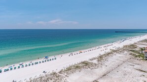 Une plage bordée de rangées de parasols et de chaises longues, une jetée s’avançant dans l’eau et un ciel dégagé.