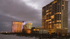 Un grand hôtel à plusieurs étages, une plage au premier plan et un ciel nuageux.