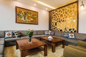 A living room with a sectional sofa, two wooden coffee tables, a decorative wall panel, and a framed painting. - Sapa Delta Hotel (Sa Pa)