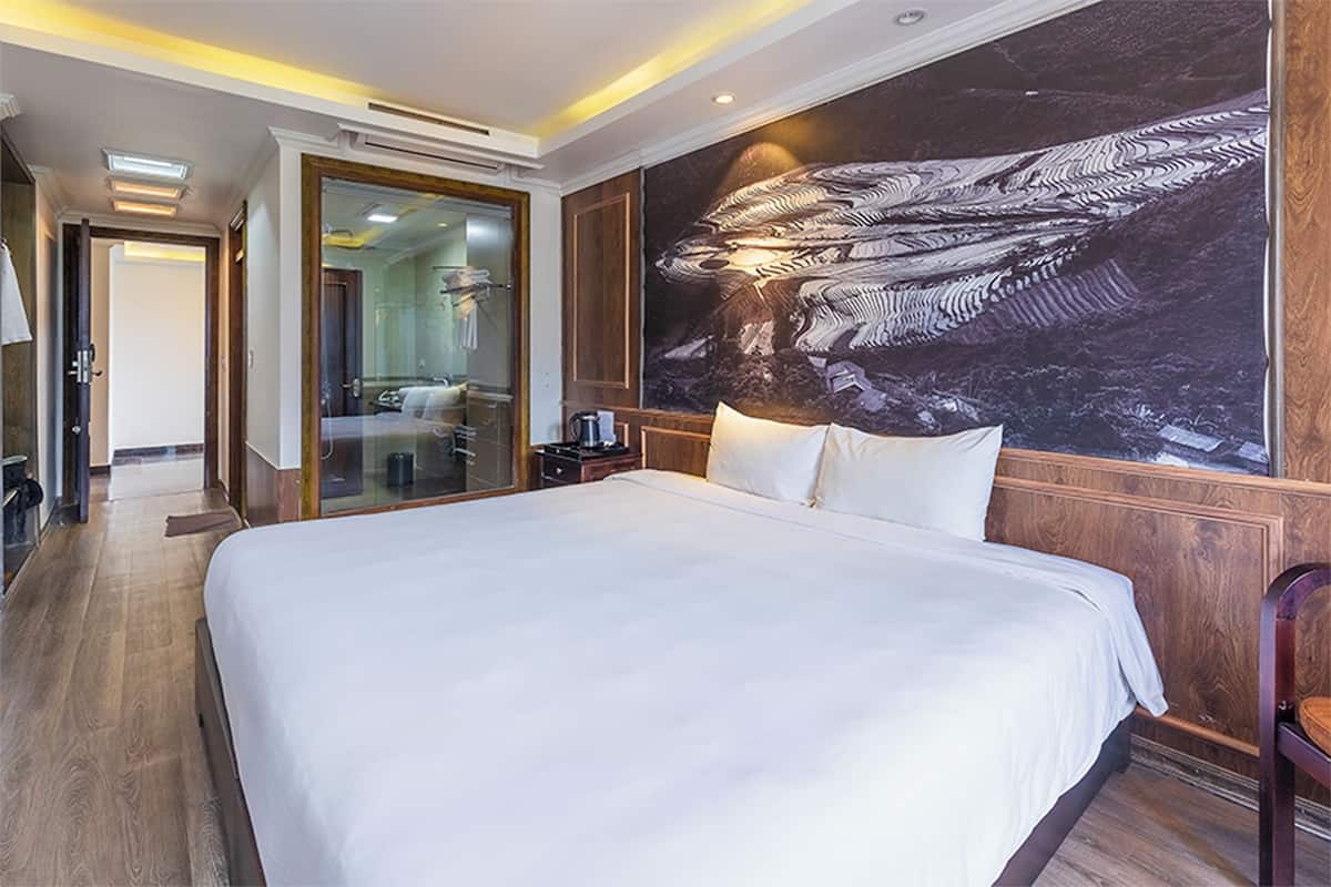 Habitación de hotel con una cama grande, paneles de madera, un mural en la pared y un baño moderno con cabina de ducha de vidrio.