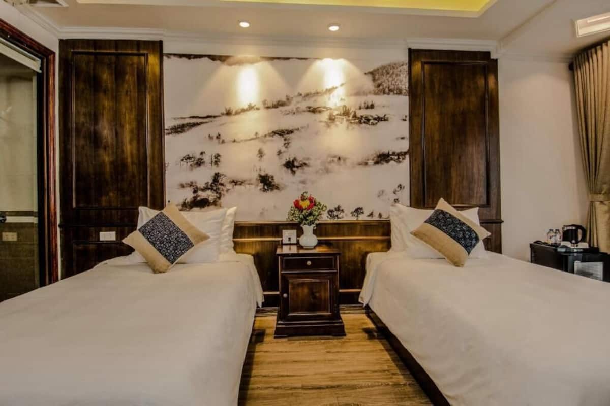 Habitación de hotel con dos camas, una mesita de noche de madera con un florero y un mural grande en la pared.
