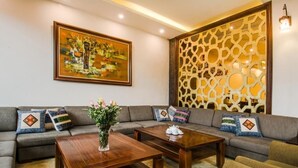 A living room with a sofa set, two wooden coffee tables, a decorative wall panel, and a framed painting. - Sapa Delta Hotel (Sa Pa)