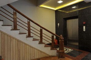 A staircase with wooden handrails and a patterned carpet leading to an elevator. - Sapa Delta Hotel (Sa Pa)