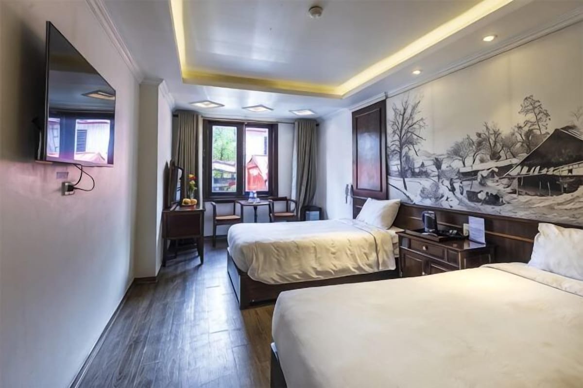 A hotel room with two beds, a desk, a chair, a TV, and a painting on the wall.