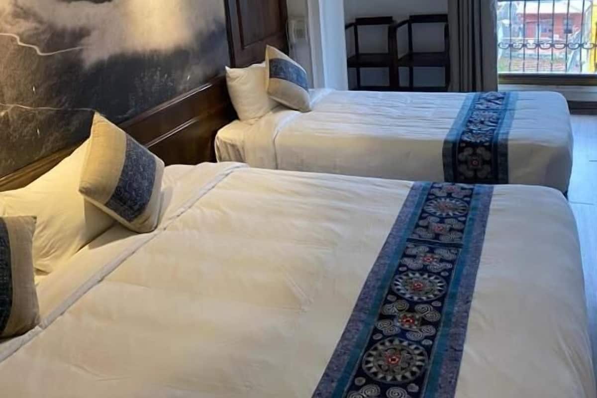Habitación de hotel con dos camas, un cuadro grande en la pared, un balcón con vistas y una mesita.