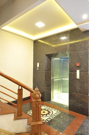 A modern elevator with a glass enclosure, a marble-tiled floor, and a wooden handrail. - Sapa Delta Hotel (Sa Pa)