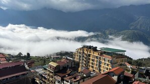 A multi-story hotel with a green roof, surrounded by mountainous terrain and clouds. - Sapa Delta Hotel (Sa Pa)