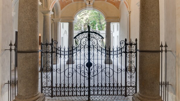 An ornate iron gate with intricate designs, flanked by columns and arches, leading to a courtyard. - Palazzo del Carretto (Turin)