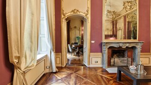 A room with a wooden parquet floor, a fireplace with a mirror above it, and a dining area in the background. - Palazzo del Carretto (Turin)