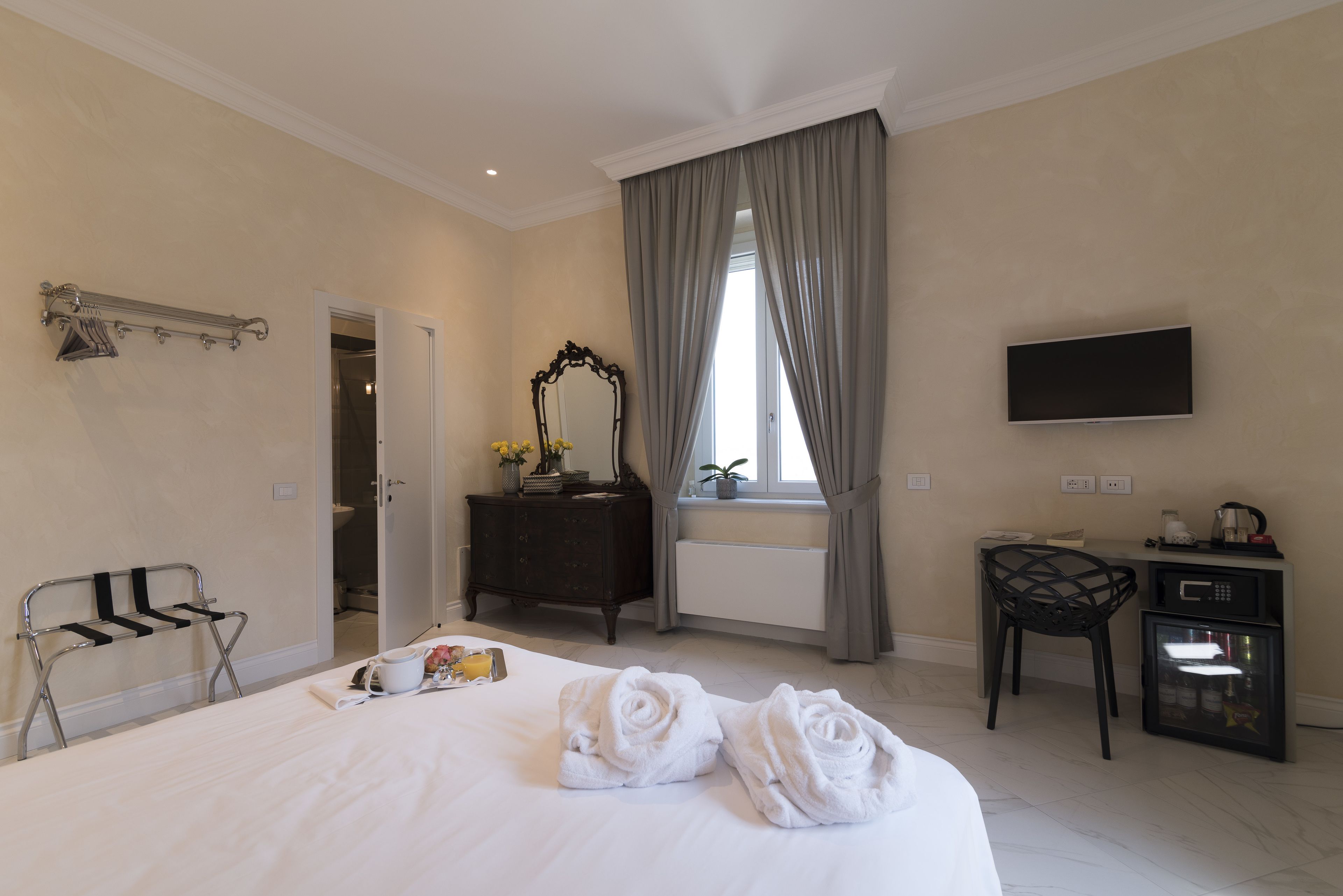 Una camera d'albergo con un letto, una scrivania, una sedia, una televisione e un bagno visibile attraverso una porta aperta.
