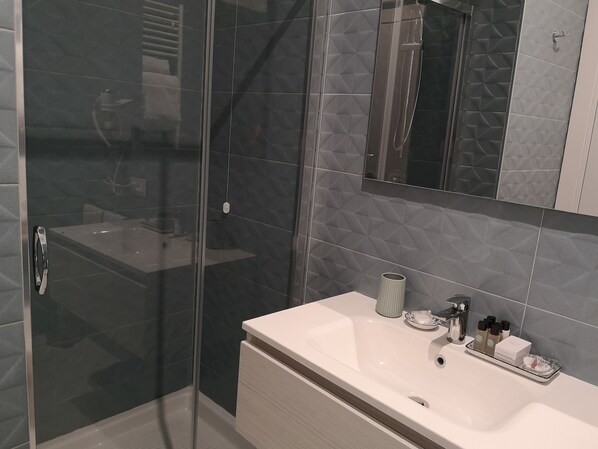 A modern bathroom with a glass shower enclosure, a white sink with a tray of toiletries, and a large mirror above the sink. - Altavilla Boutique Hotel (Catanzaro)