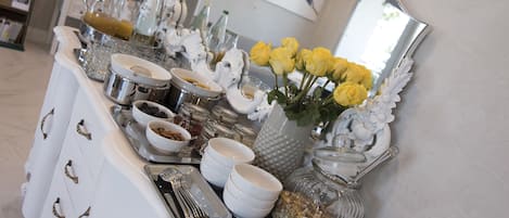 A buffet setup with white dishes, a glass jar, and yellow roses.
