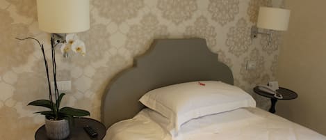 Habitación de hotel con una cama, dos mesitas de noche, una lámpara en cada mesita y una planta en maceta, además de una pared con estampado floral.