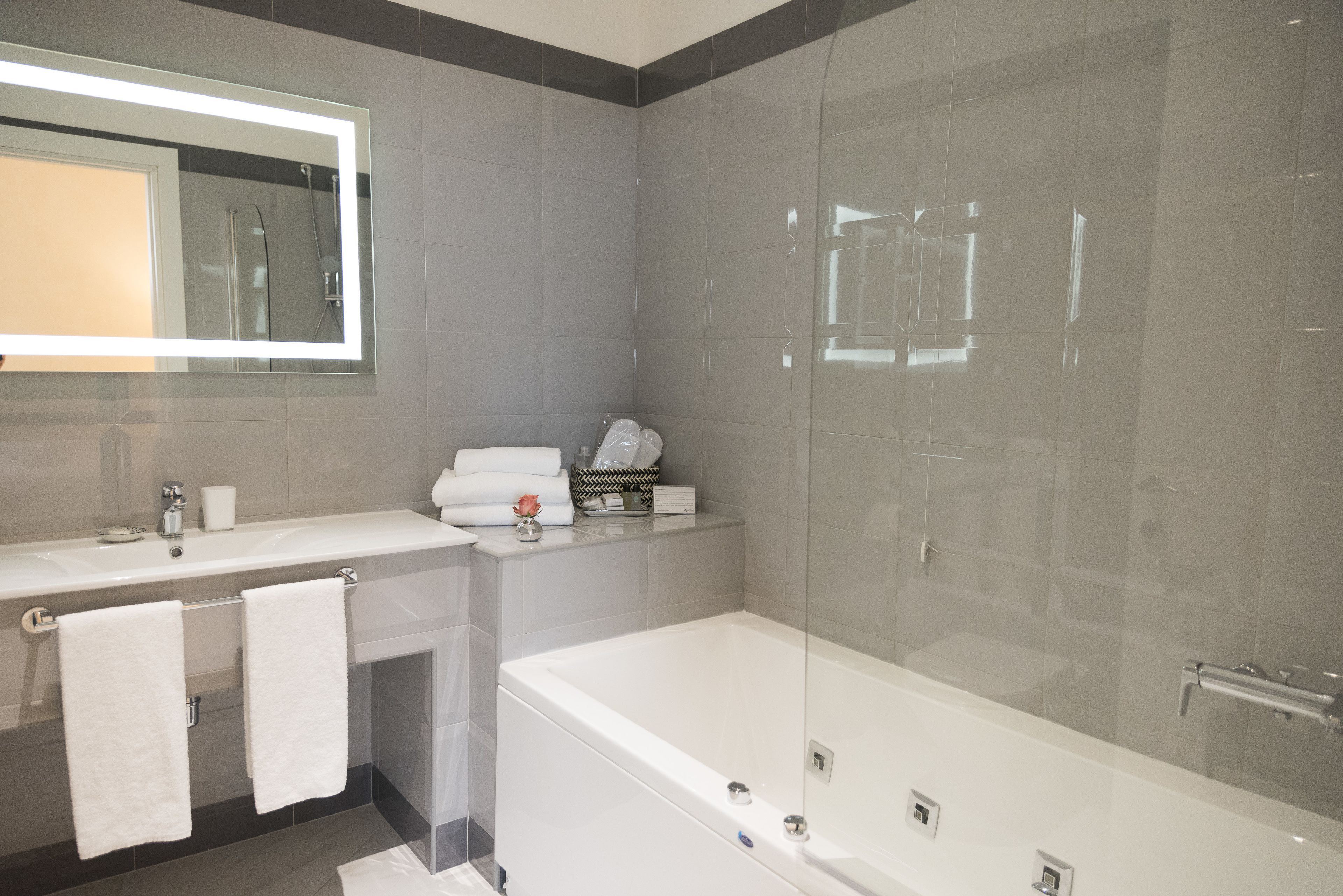 A modern bathroom with a large mirror, two sinks, a bathtub, and a glass-enclosed shower.