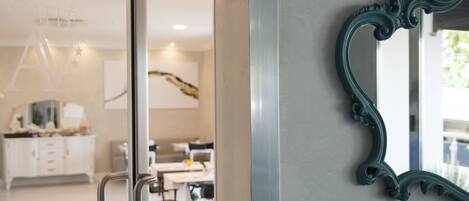 A modern interior with a glass door leading to a dining area, a decorative mirror, and a ceiling with recessed lighting.