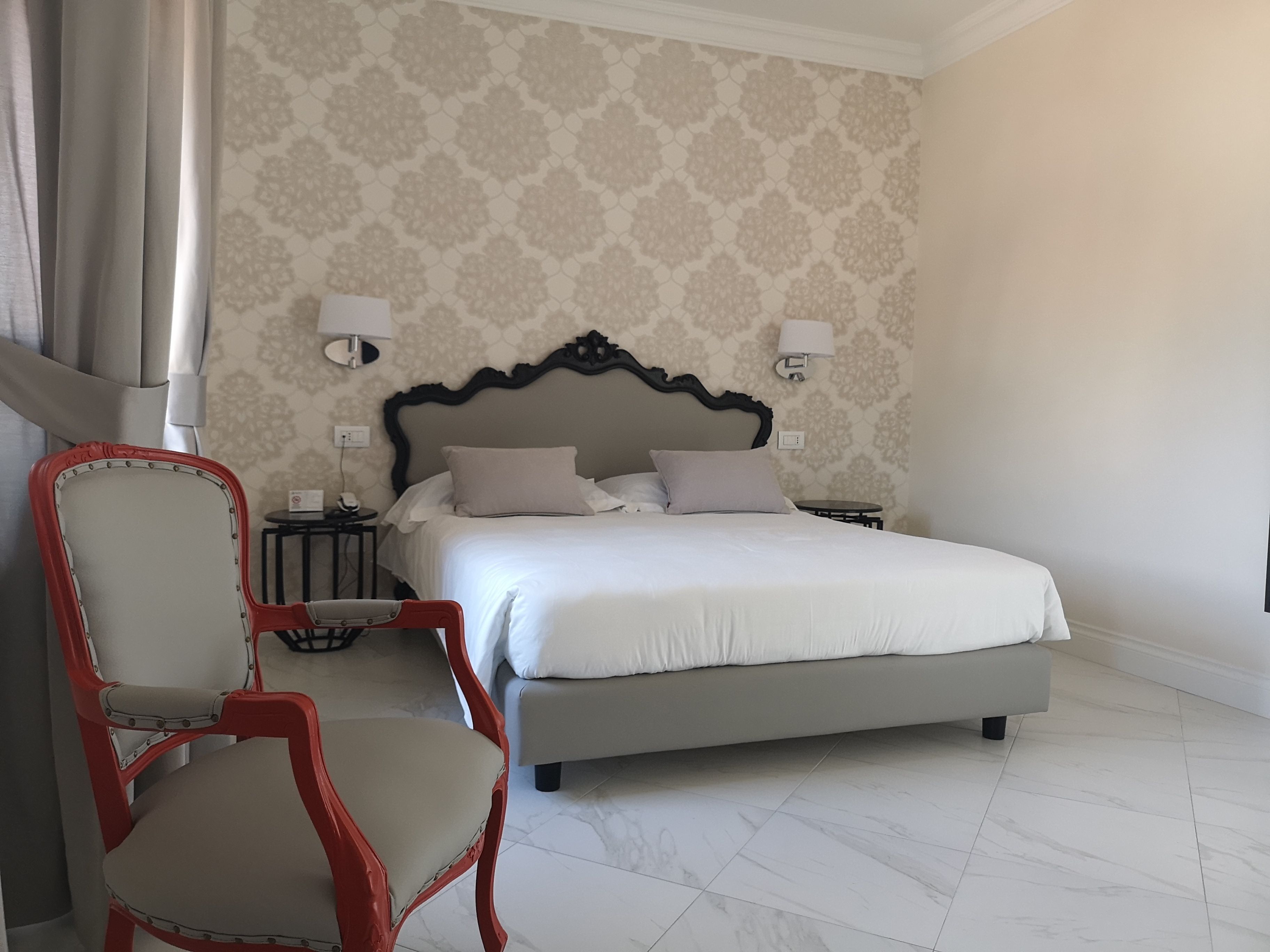 A neatly arranged bedroom with a large bed, a chair, a nightstand, and a wall-mounted lamp.
