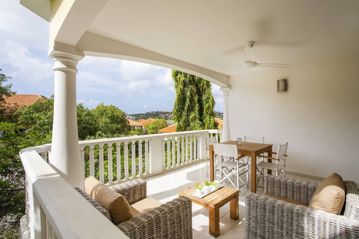 A balcony with wicker furniture, a wooden table, and a ceiling fan.