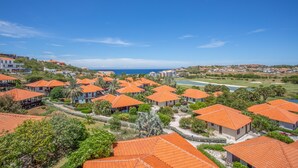 Un complex turístic amb diversos edificis de teulades taronja, envoltat de vegetació i una vista despejada de l'oceà.