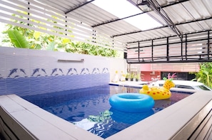 Une piscine dont l’un des murs est recouvert de carreaux décorés de motifs de dauphins, avec un anneau gonflable bleu et un canard gonflable jaune.
