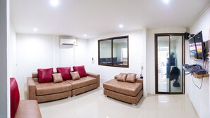 Uma sala de estar moderna com um sofá marrom, uma poltrona vermelha e uma porta de vidro que dá para uma varanda.