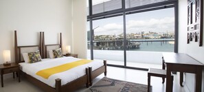 A hotel room with a large window, a bed with a yellow throw, a desk, and a chair. - Hotel Englishpoint Marina (Mombasa)