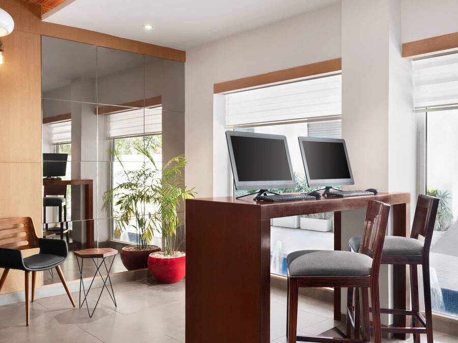 Un espace de bureau moderne avec un bureau en bois, deux écrans d’ordinateur, un téléphone et une plante en pot.