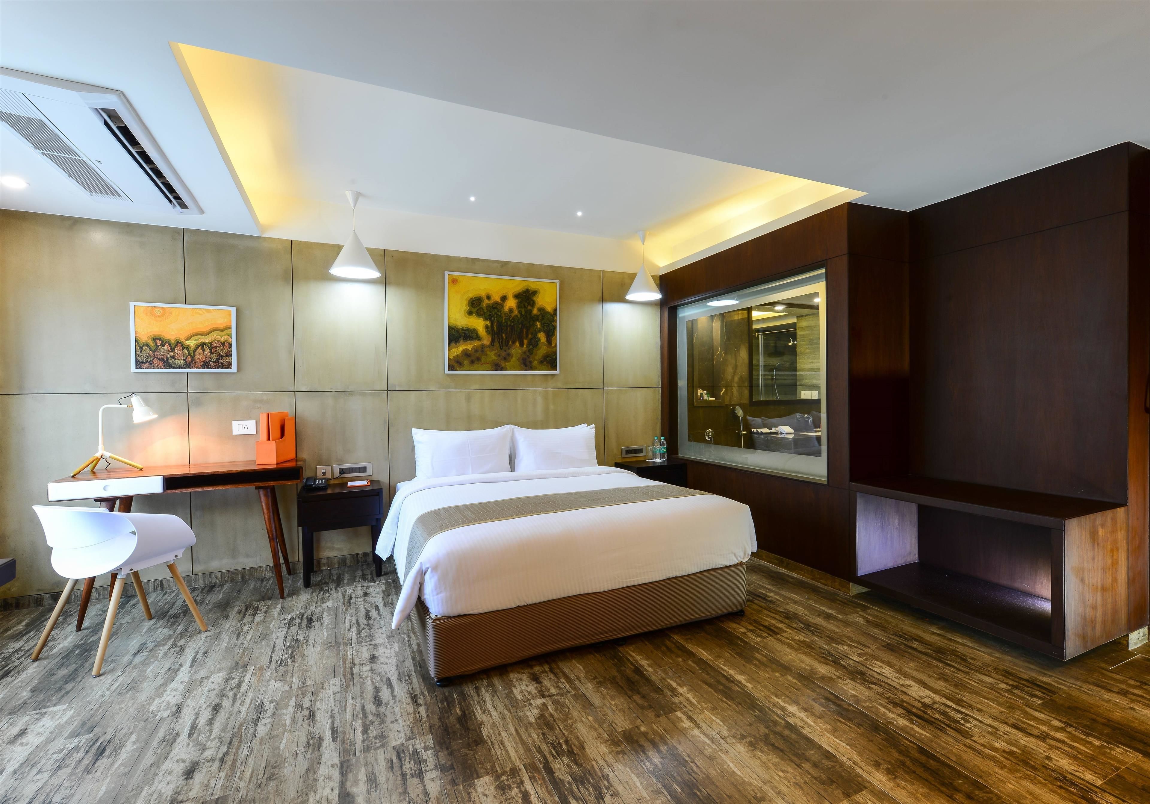 A modern hotel room with a large bed, a desk, a chair, and a large window.