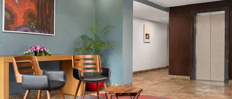 Un espace d’accueil avec un bureau en bois, deux chaises, une plante en pot et un tapis coloré.