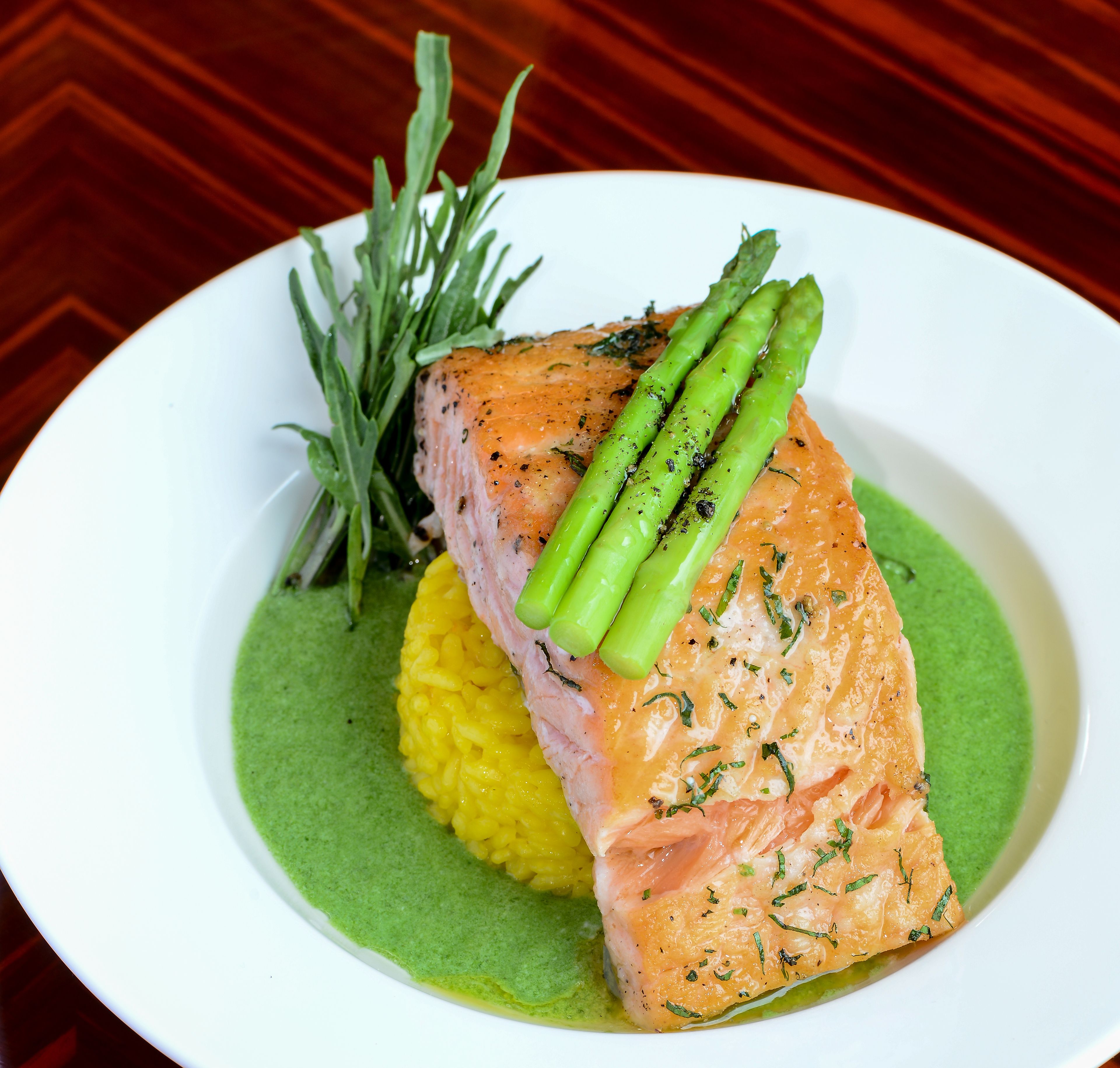 A plate with salmon, asparagus, and a green sauce.