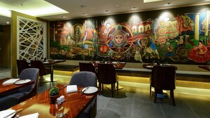 A restaurant with a mural depicting various cultural scenes, wooden tables with chairs, and a modern interior design.
