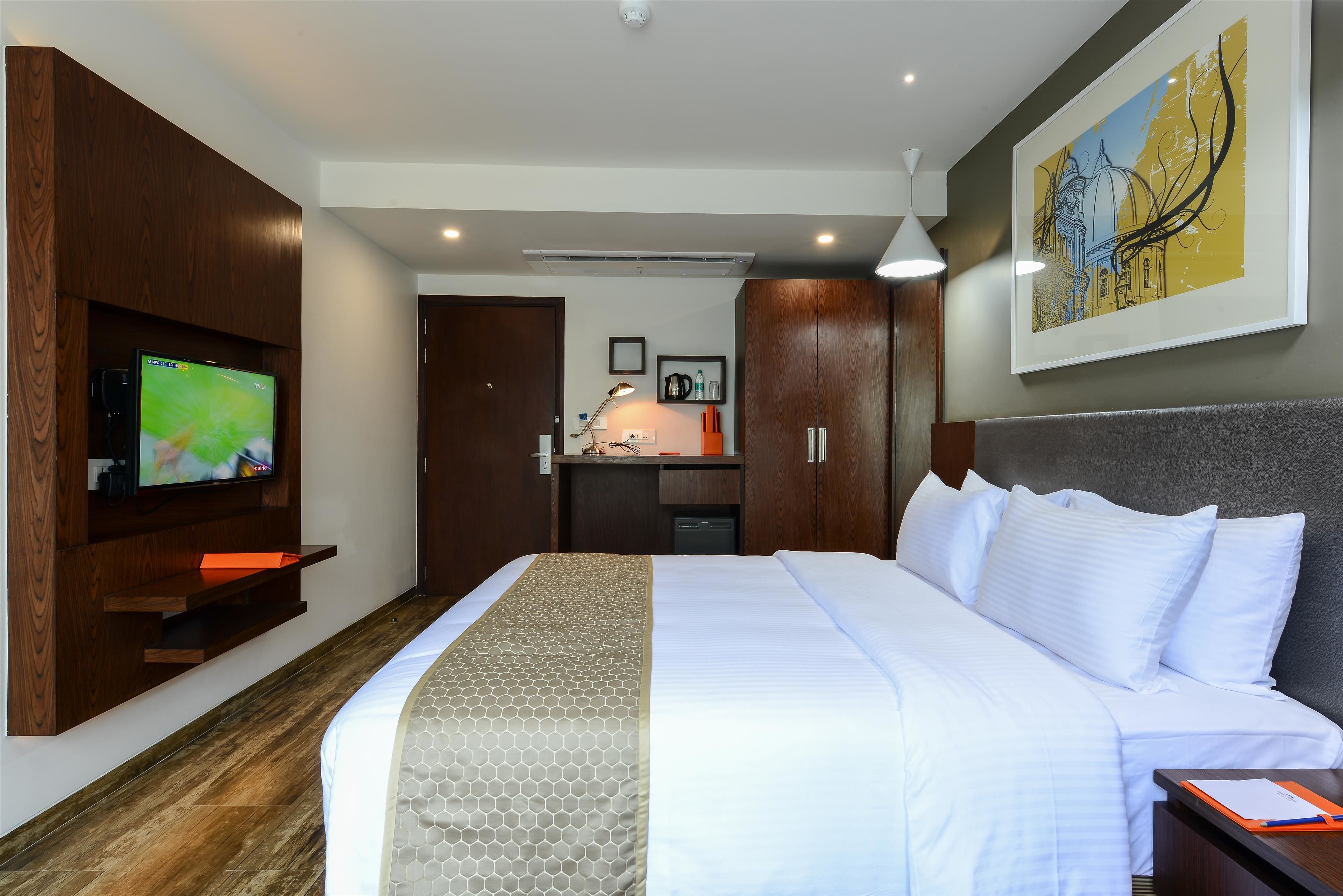 Ein Hotelzimmer mit einem großen Bett, einem Fernseher, einem Schreibtisch mit Lampe und einem Bild an der Wand.