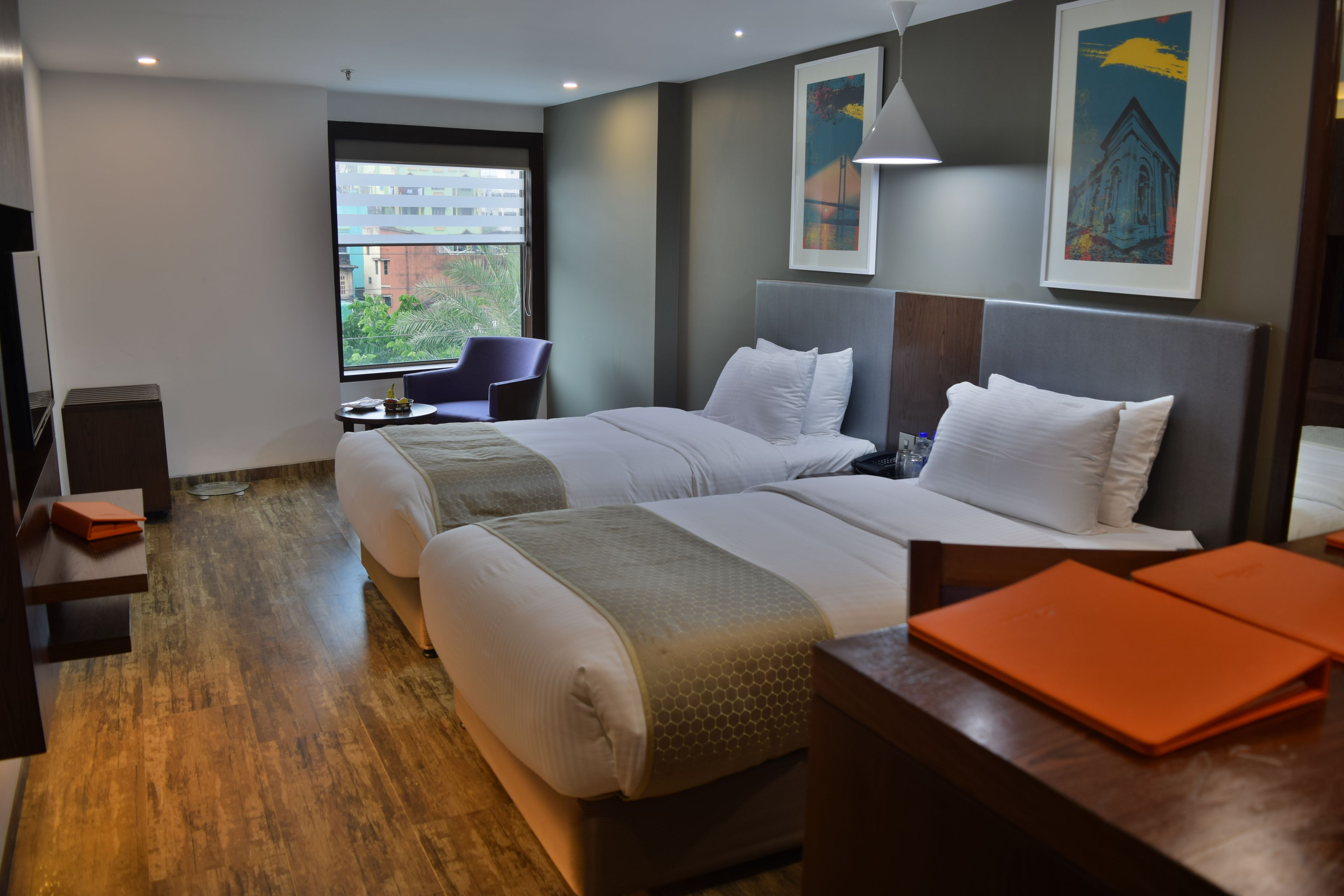 Habitación de hotel con dos camas, un escritorio, una silla y una ventana con vista a edificios.